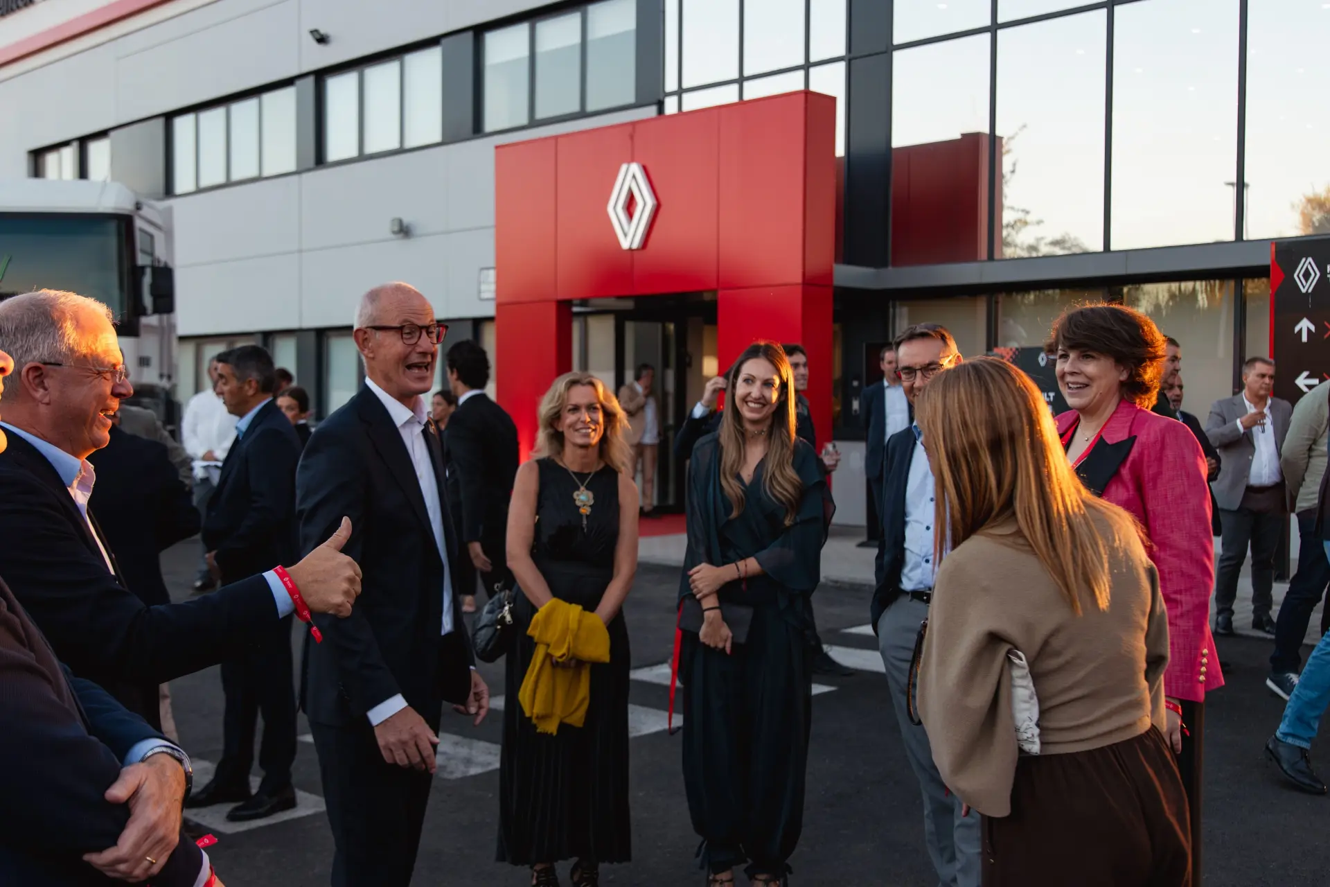Un grupo de personas sonríe y charla frente a un edificio moderno con un letrero rojo con el logotipo de Renault en Getafe, lo que pone de manifiesto su compromiso con el transporte profesional y un excelente servicio posventa.