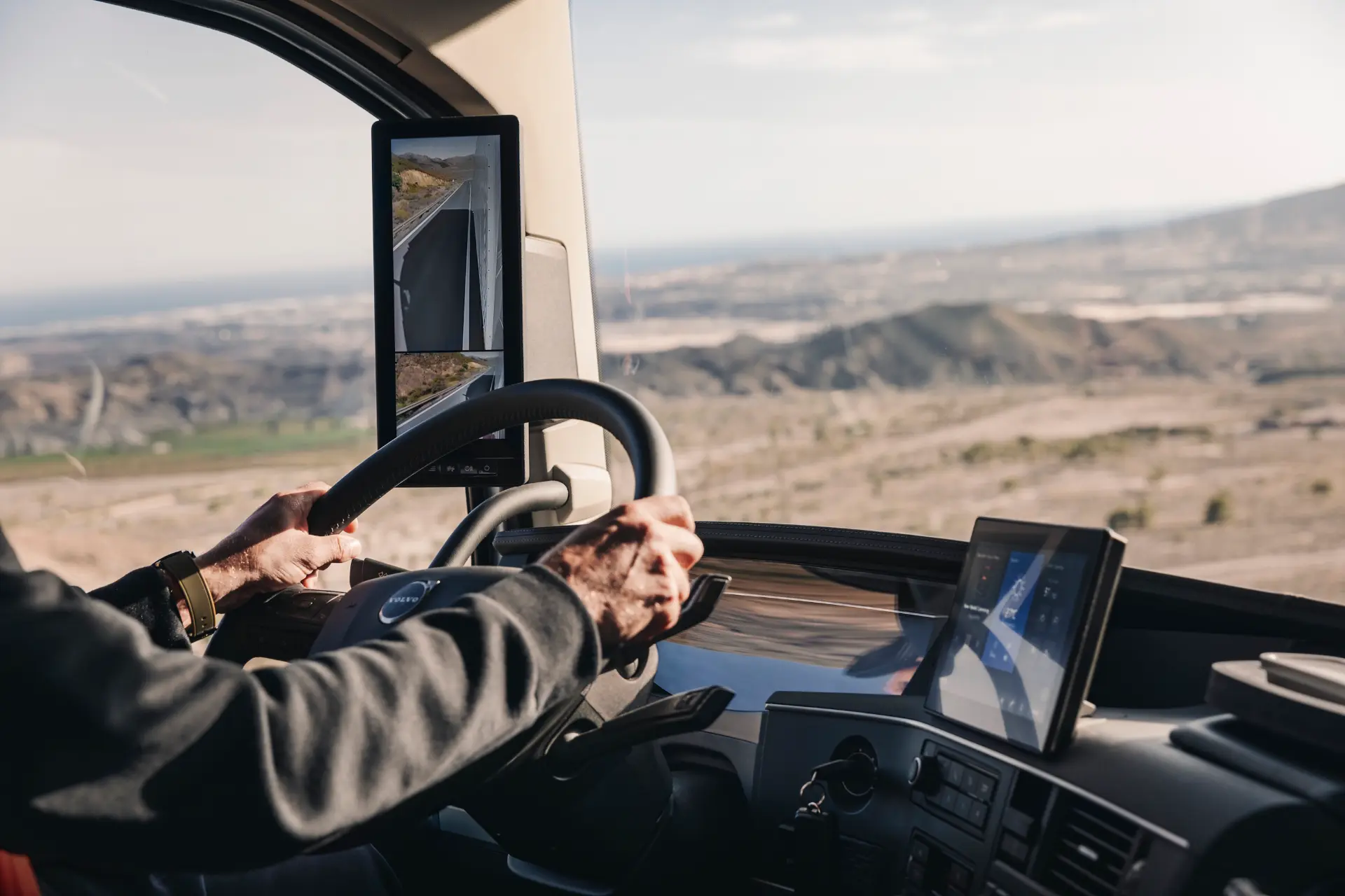 Las manos sobre el volante de un camión, con vistas a un paisaje desértico cerca de un borrador eléctrico.