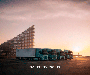 Cuatro camiones Volvo aparcados frente a un edificio moderno al amanecer para este banner de escritorio.