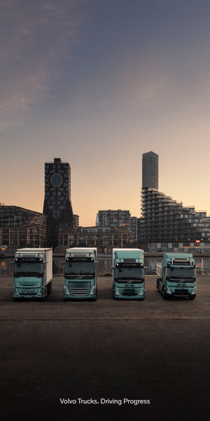 Cuatro camiones eléctricos Volvo aparcados frente al perfil urbano de la ciudad al atardecer para un banner web.