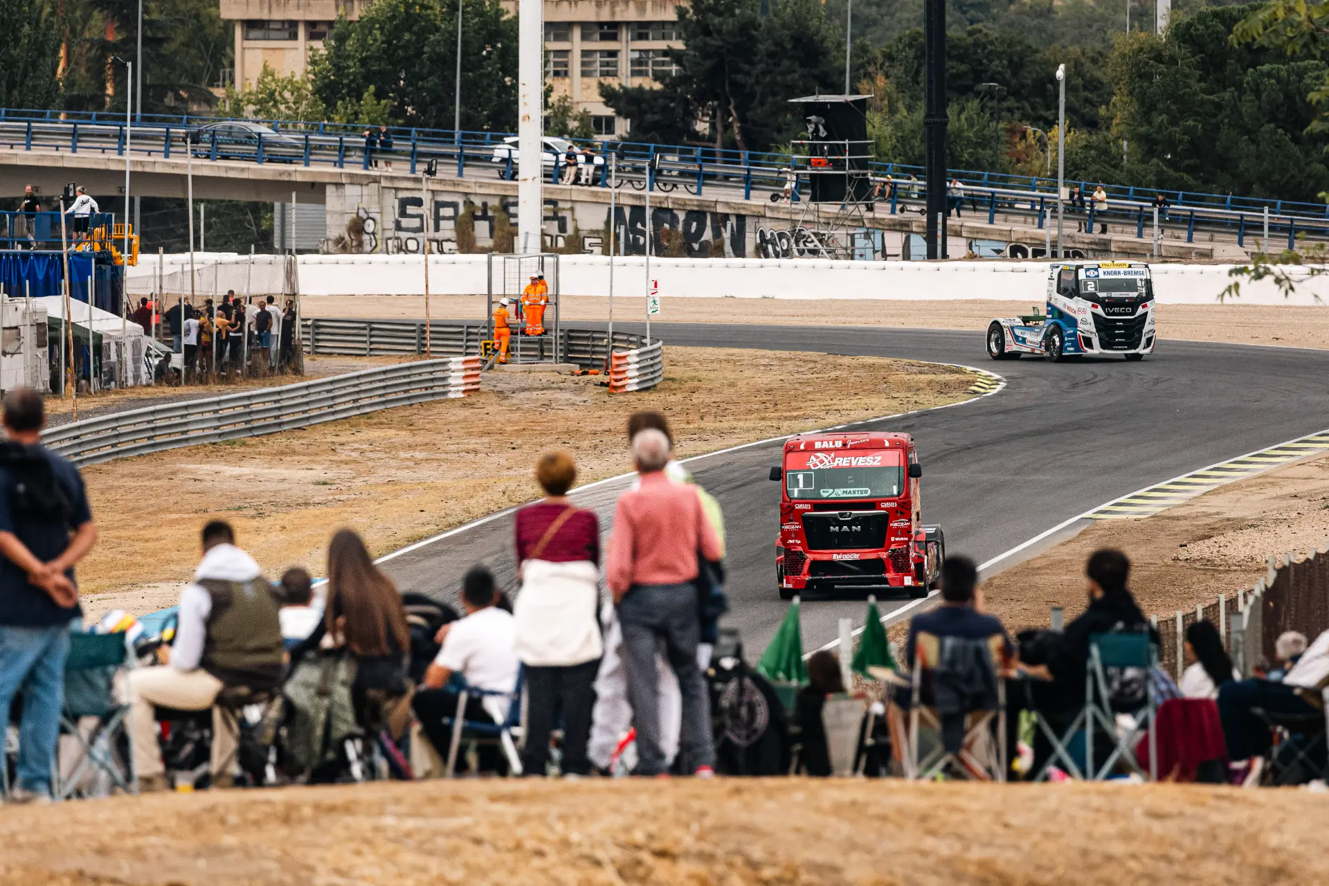 Dos camiones de carreras compiten en el circuito del Europeo de Camiones, vistos desde detrás de los espectadores.