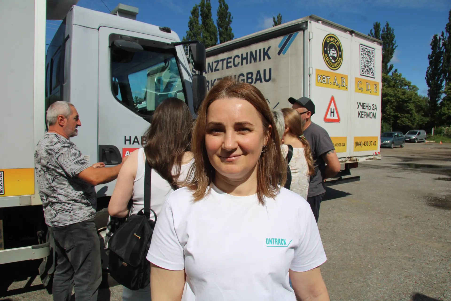 Una camionera ucraniana con una camiseta blanca con el logotipo de la marca, de pie delante de unos camiones aparcados.