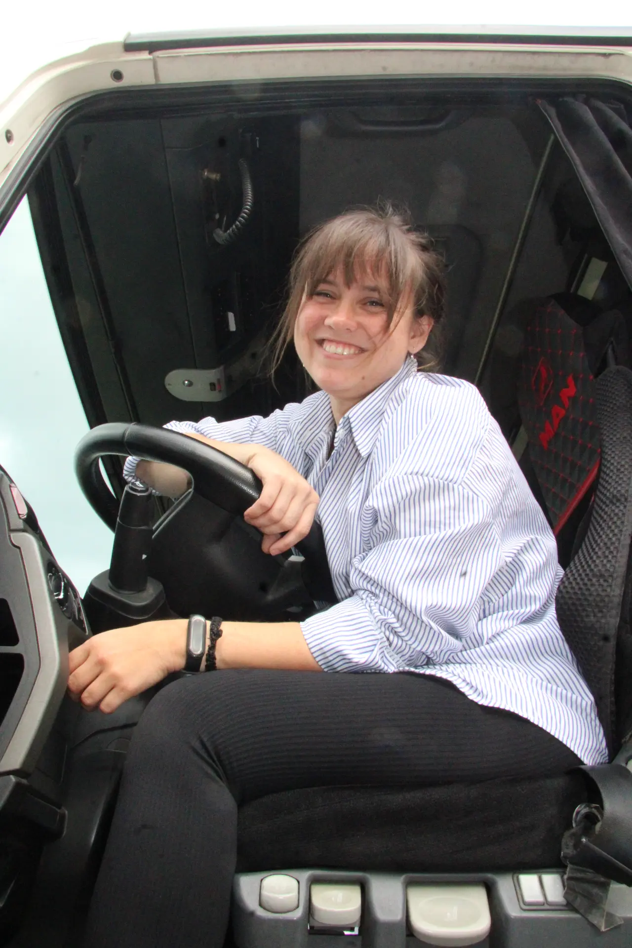 Una mujer sonriente sentada en el asiento del conductor de un camión, que representa a las mujeres camioneras.